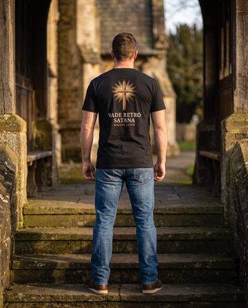 Man seen from behind in a tee whose back print shows an engraved cross in golden rays over VADE RETRO SATANA