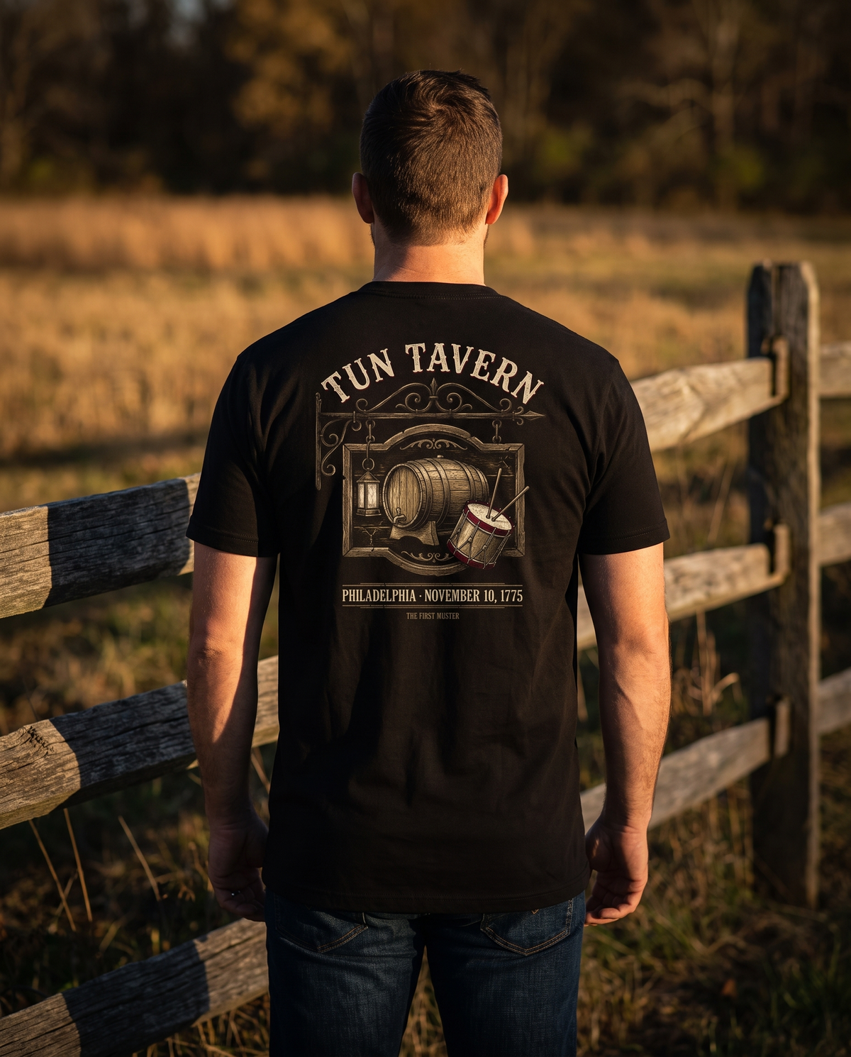 Man seen from behind in a black tee whose back print shows the Tun Tavern sign with cask, lantern and drum, November 10, 1775