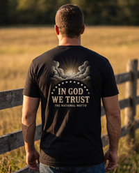 Man seen from behind wearing the In God We Trust shirt: sunburst through engraved clouds, an arc of stars, bold motto &mdash; view 1