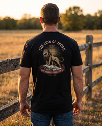 Man seen from behind wearing a Lion of Judah tee: a lion on a rock before a crowned cross, Revelation 5:5 banner &mdash; view 1