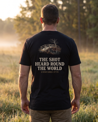 Man seen from behind wearing a tee with an engraved wooden footbridge over The Shot Heard Round the World, Concord 1775 &mdash; view 1
