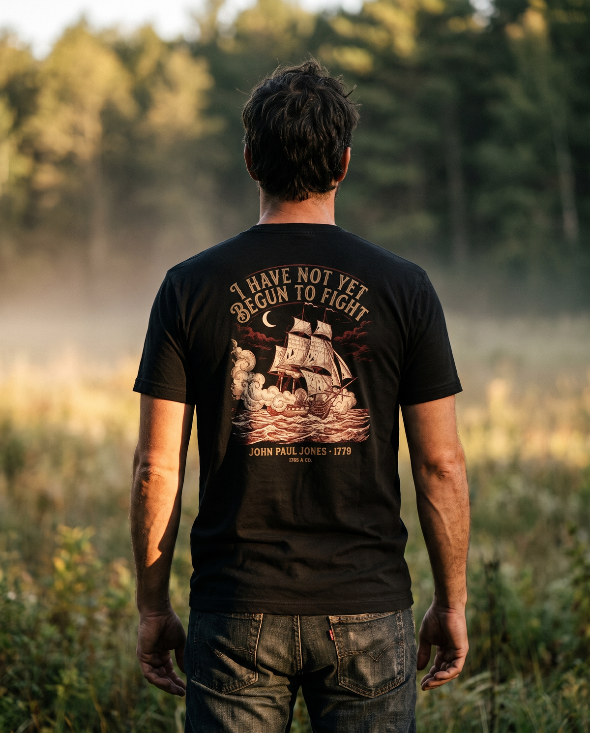 Man seen from behind wearing the tee: an engraved warship in cannon smoke under 'I Have Not Yet Begun to Fight'
