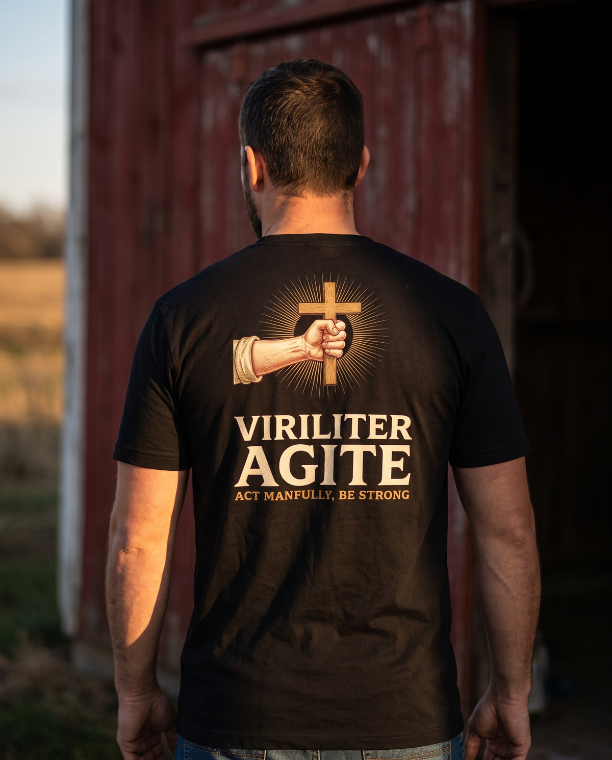 Man seen from behind in a 1765 Apparel tee; back print: a fist gripping a wooden cross in gold rays, Viriliter Agite