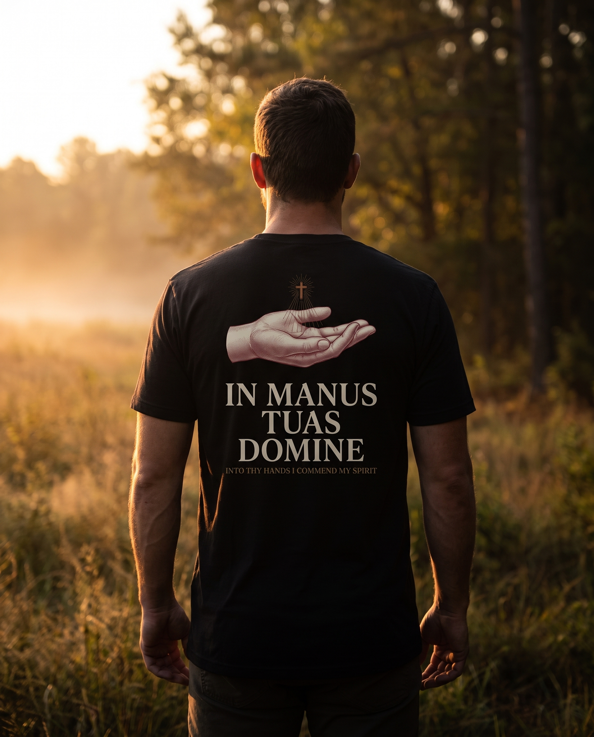 Man seen from behind in a 1765 Apparel tee; back print: an open hand beneath a radiant cross, In Manus Tuas Domine
