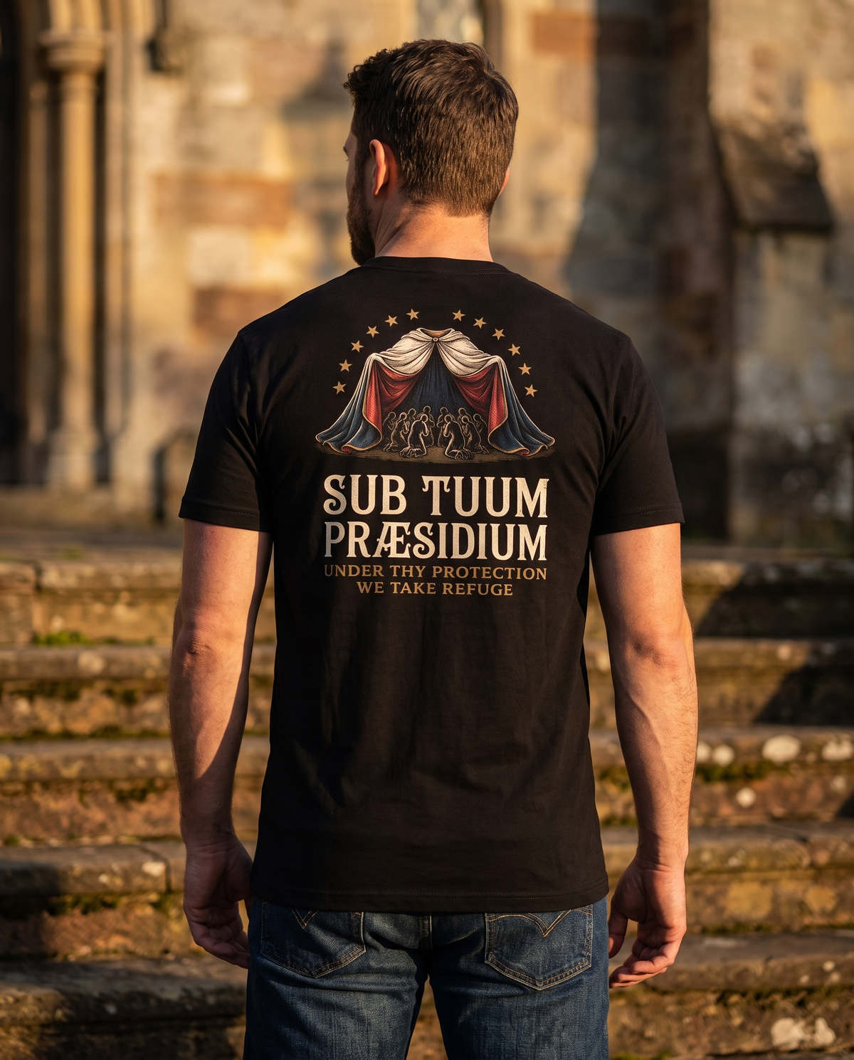 Man seen from behind in a 1765 Apparel tee; back print: a mantle over kneeling faithful, twelve stars, Sub Tuum Praesidium