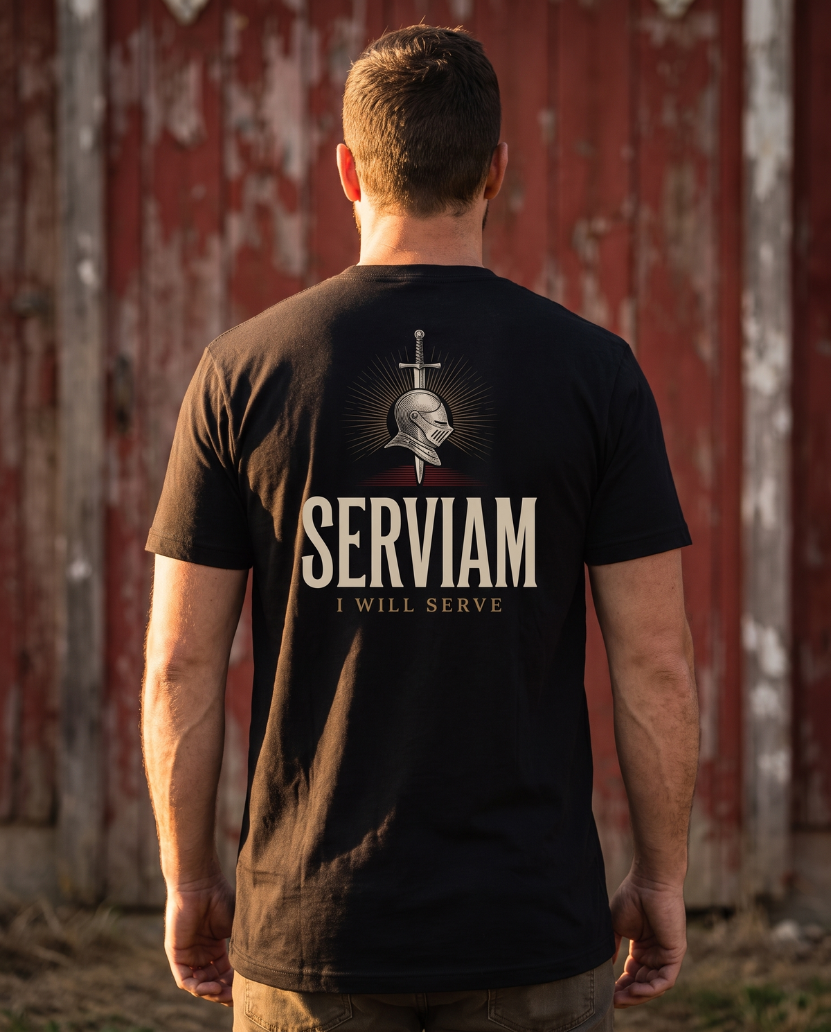 Man seen from behind in a 1765 Apparel tee; back print: knight's helm and sword in gold rays, Serviam, I Will Serve