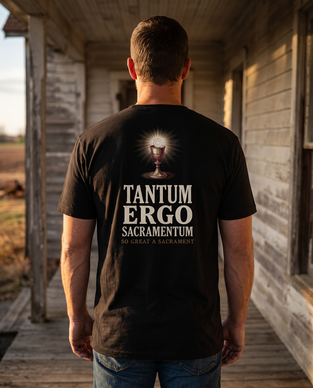 Man seen from behind in a tee whose back print shows a gold chalice and radiant Host over TANTUM ERGO SACRAMENTUM